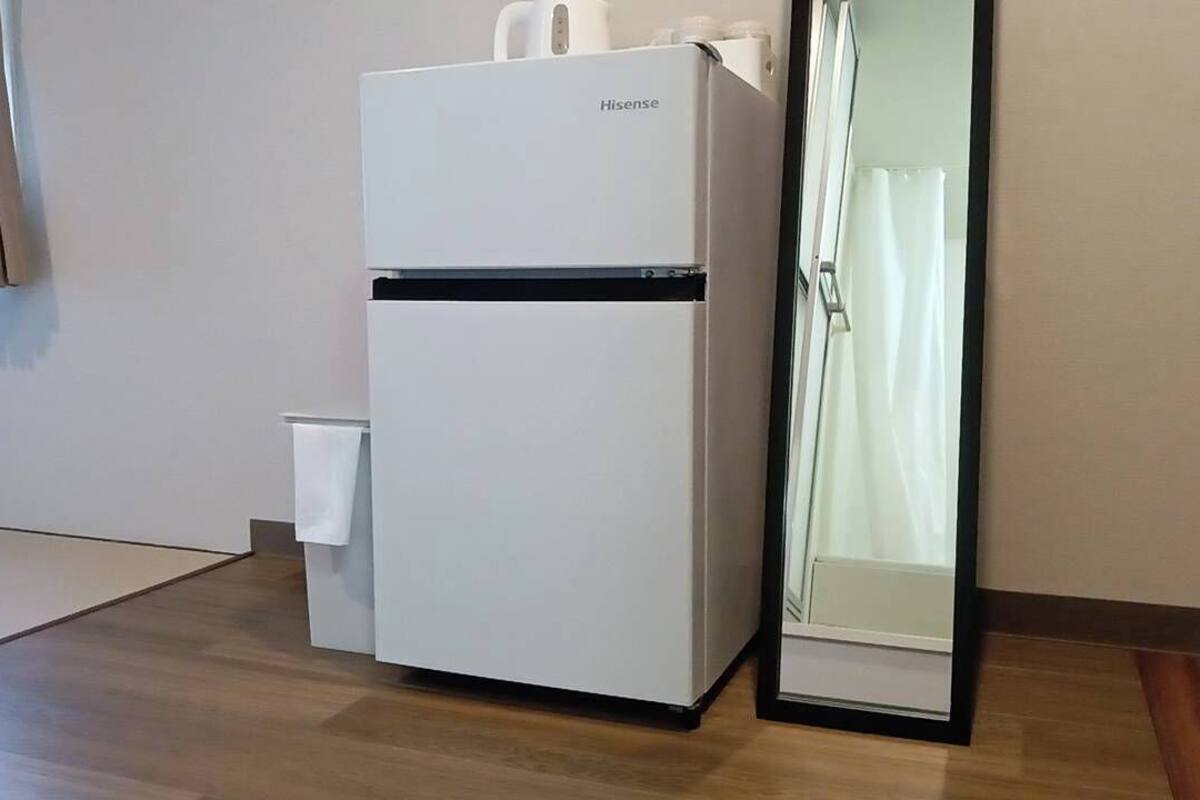 A compact, white Hisense refrigerator with a freezer compartment, positioned next to a glass door cabinet.