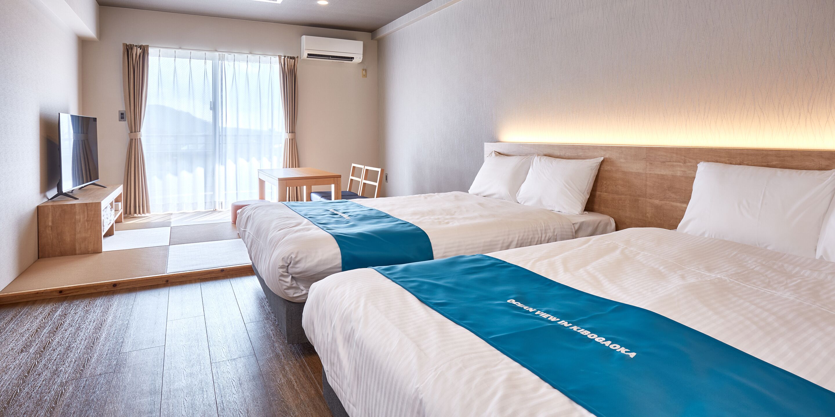 A hotel room with two beds, a TV, a small table, and a chair.