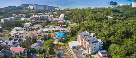 Vue aérienne d’un quartier résidentiel situé sur la côte, avec différents bâtiments, dont un hôtel doté d’un toit rouge et une grande bâche bleue recouvrant un chantier de construction.