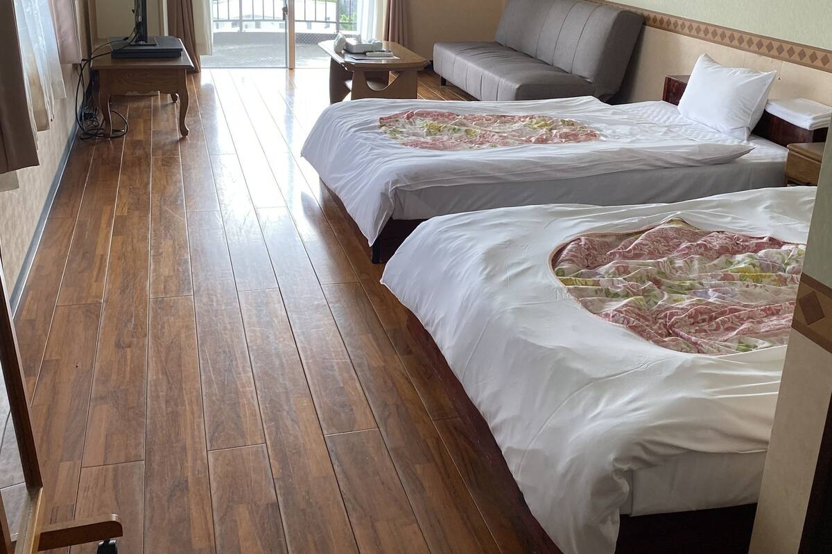 A hotel room with two beds, a sofa, a small table, an air conditioning unit, and a view of the outdoors.