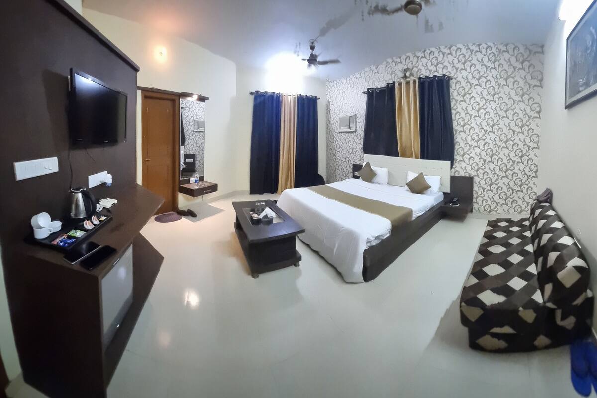 A hotel room with a bed, a desk, a TV, and a wall-mounted heater.