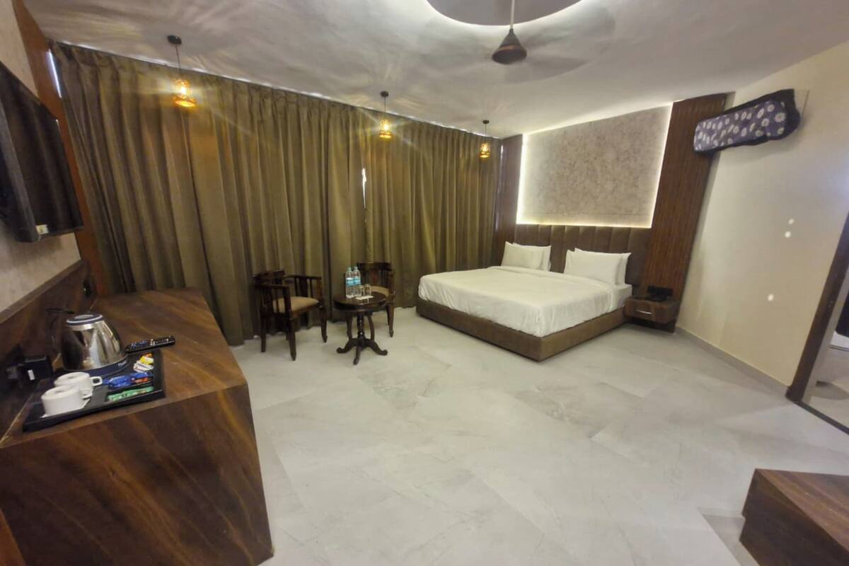 A hotel room with a bed, a desk with a coffee maker, chairs, and a TV on the wall.