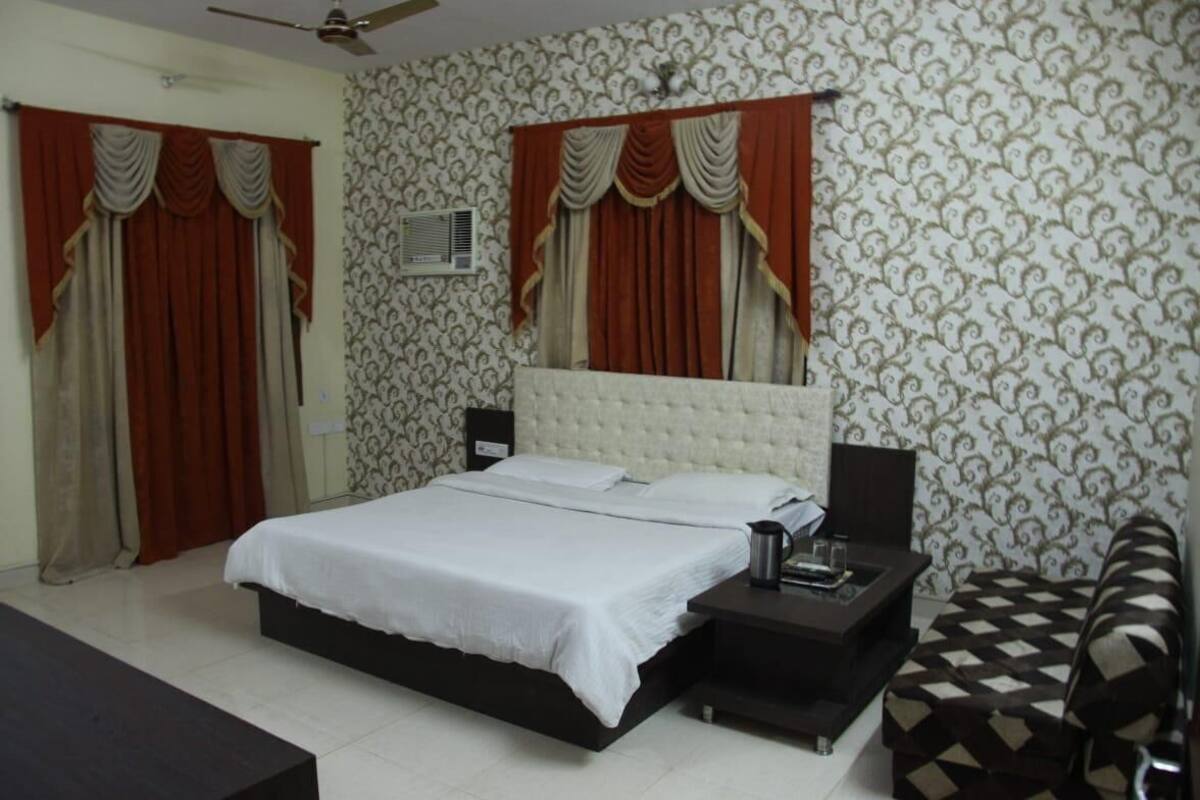 A bedroom with a bed, curtains, a nightstand, a chair, and a patterned wallpaper.