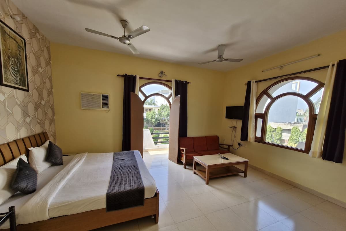 A hotel room with a bed, a sofa, a table, two ceiling fans, and large windows with curtains.