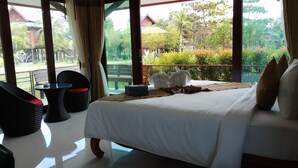 A hotel room with a bed, a small table, and chairs. There is a balcony with a view of the garden and buildings. - Villa Warin Khao Lak (Takua Pa)