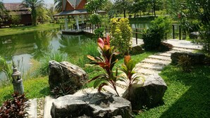 A serene garden with a pond, large rocks, and a traditional building with a sloped roof in the background. - Villa Warin Khao Lak (Takua Pa)