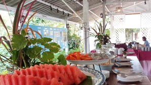 A buffet setup with a large plate of watermelon slices, various food items, and a blue informational board in the background. - Villa Warin Khao Lak (Takua Pa)