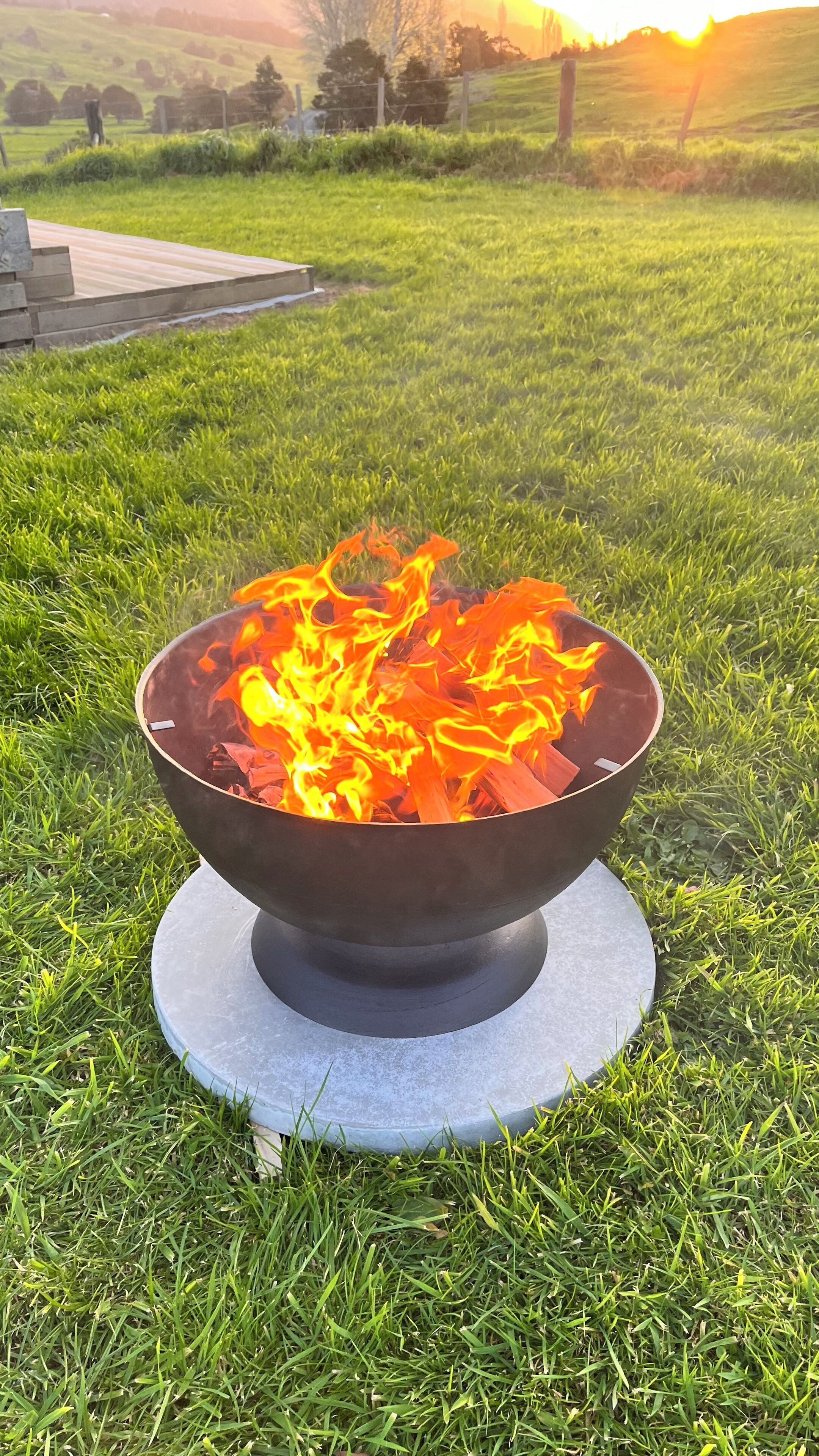 A metal fire bowl with flames on a grassy lawn.