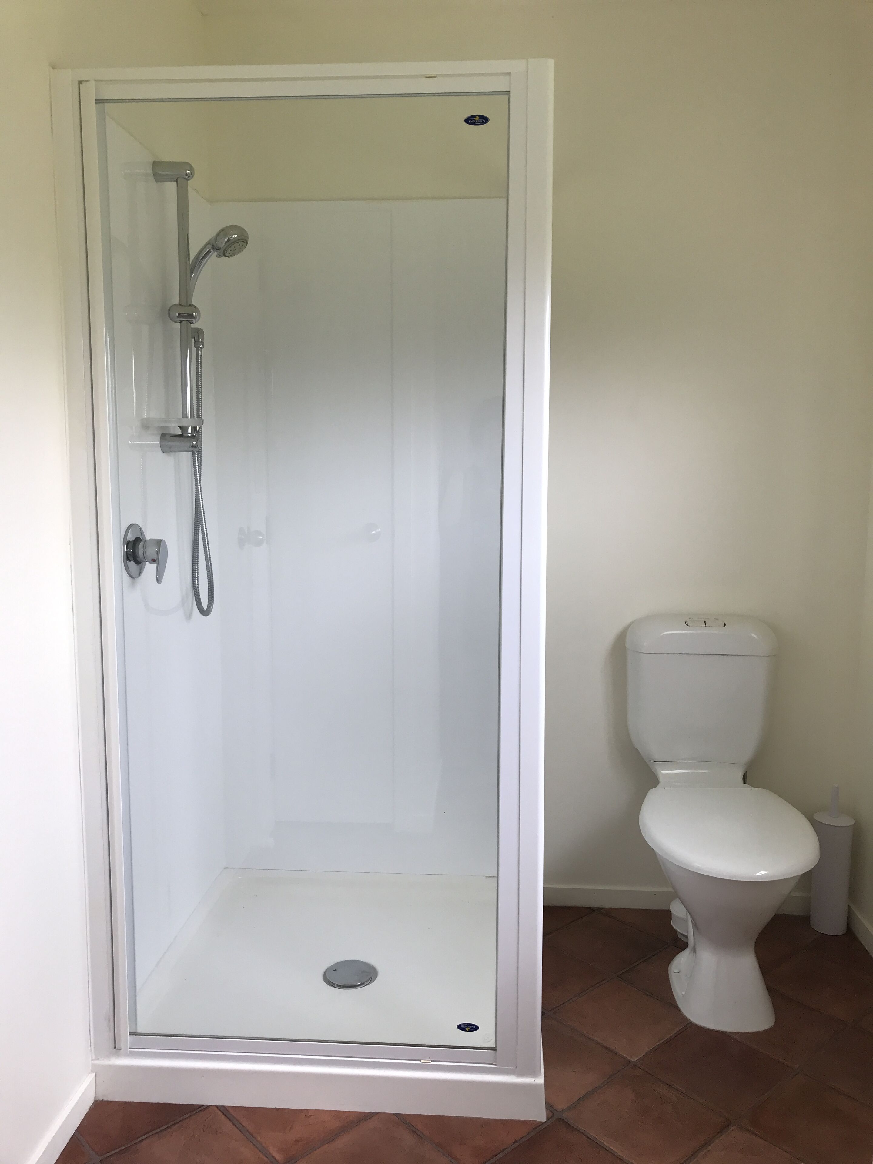 A bathroom with a glass-enclosed shower, a white toilet, and a tiled floor.