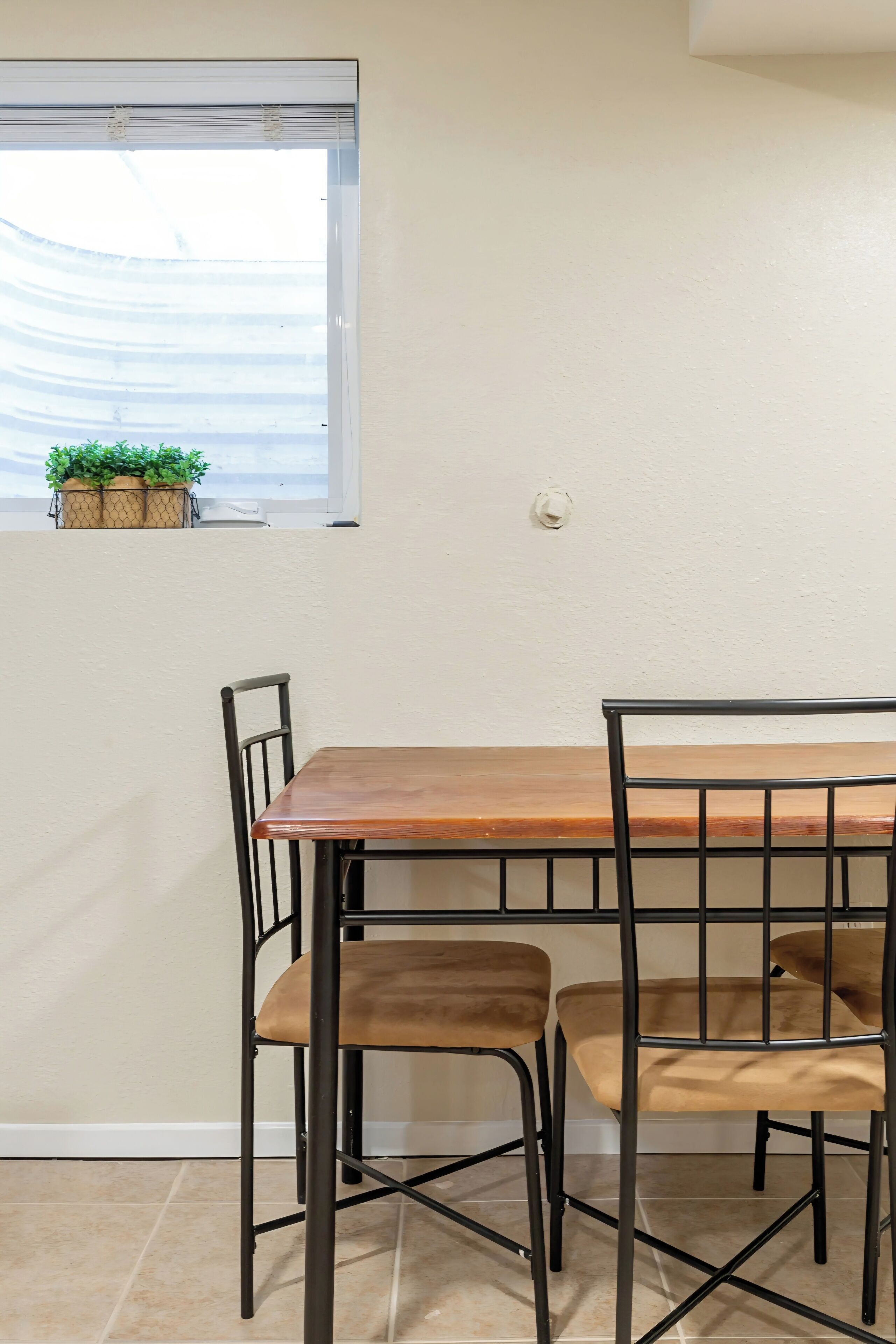 Un coin repas avec une table en bois et des chaises en métal, une fenêtre ornée de plantes en pot et un mur blanc.
