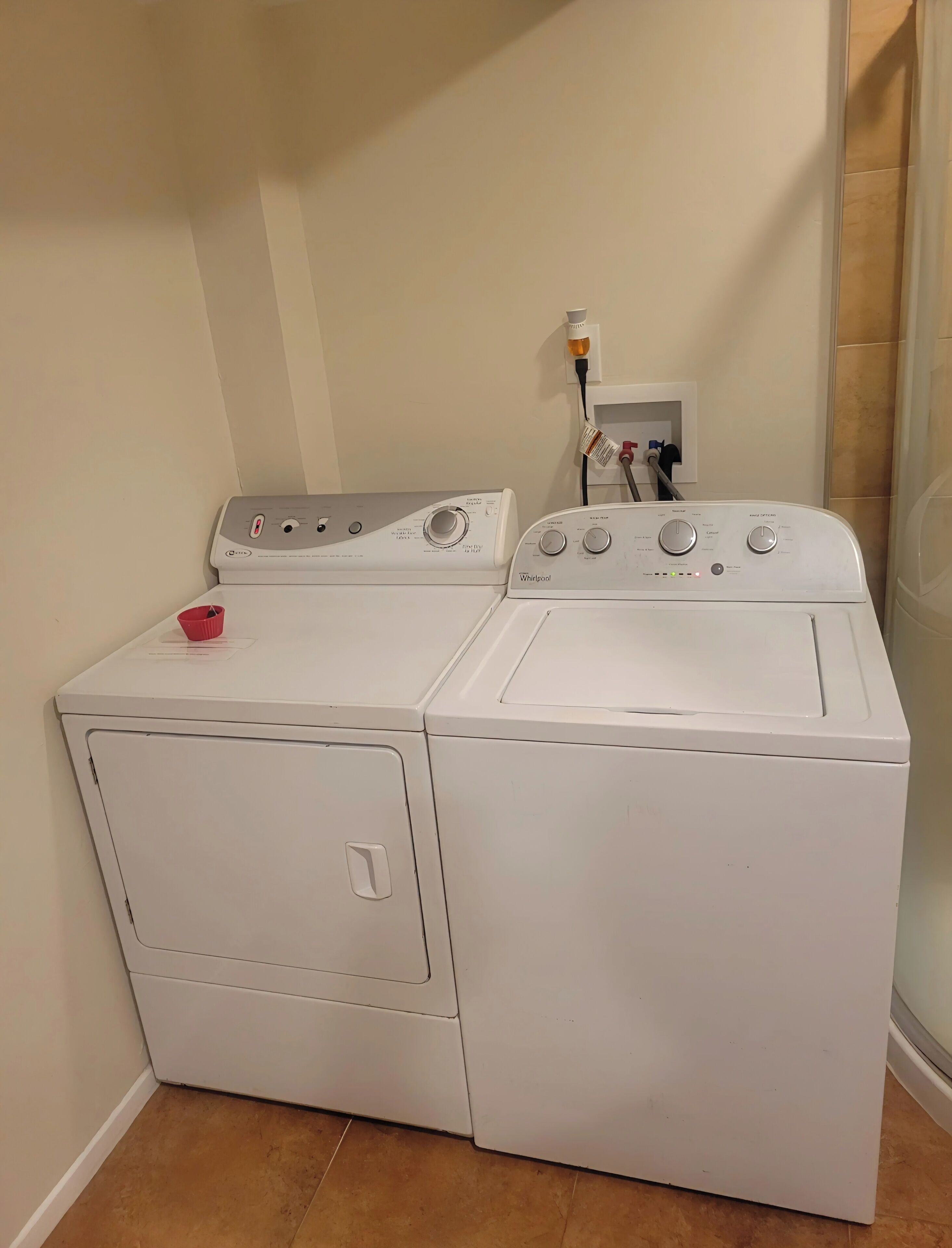 Une buanderie avec deux machines à laver et deux sèche-linge superposés, une tasse rouge posée sur la machine à laver du dessus, et une prise de courant avec un câble branché.