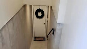 Una escalera de madera que lleva a una puerta con un adorno de laurel negro.