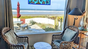 A room with wicker chairs, a small round table, and a view of the beach through a large window.