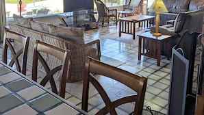 A spacious living room with a large TV, comfortable seating, and a view of the ocean through large windows.