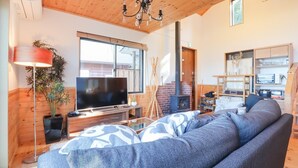A cozy living room with a large sofa, a flat-screen TV, a wooden ceiling, and a fireplace. - Ocean View House (Atami)