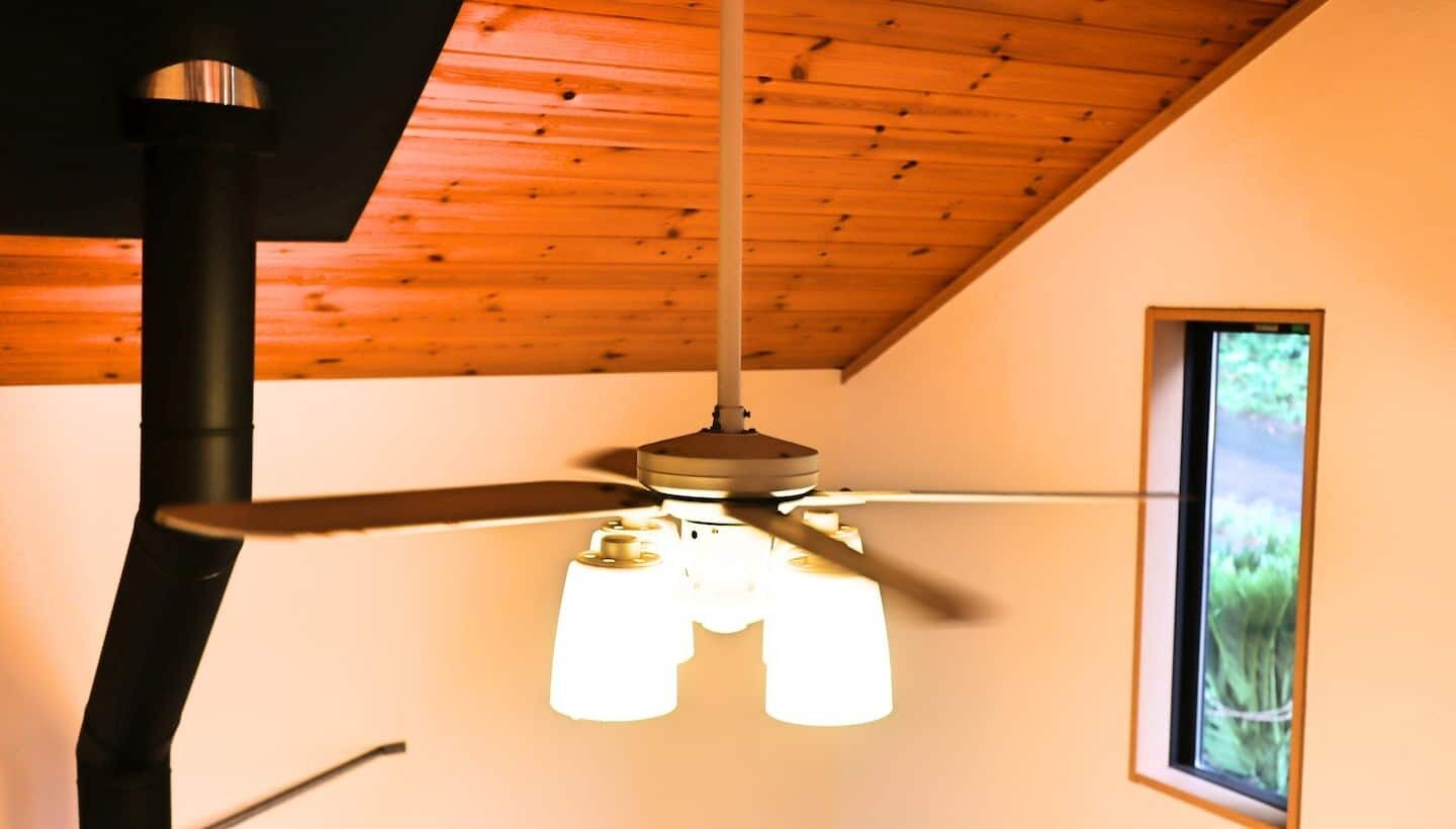 A ceiling fan with three blades and a light fixture in a room with wooden beams and a window.