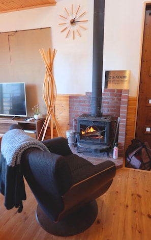 Una habitación acogedora con chimenea, televisión y un cartel que indica la ubicación como Izu-Atami.