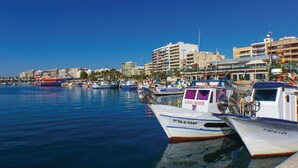 A marina with various boats docked, a clear blue sky, and buildings in the background.