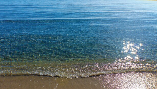 A beach with clear water and a distant pier.