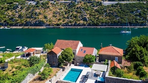 A coastal villa with a swimming pool, stone buildings, and a view of the sea.