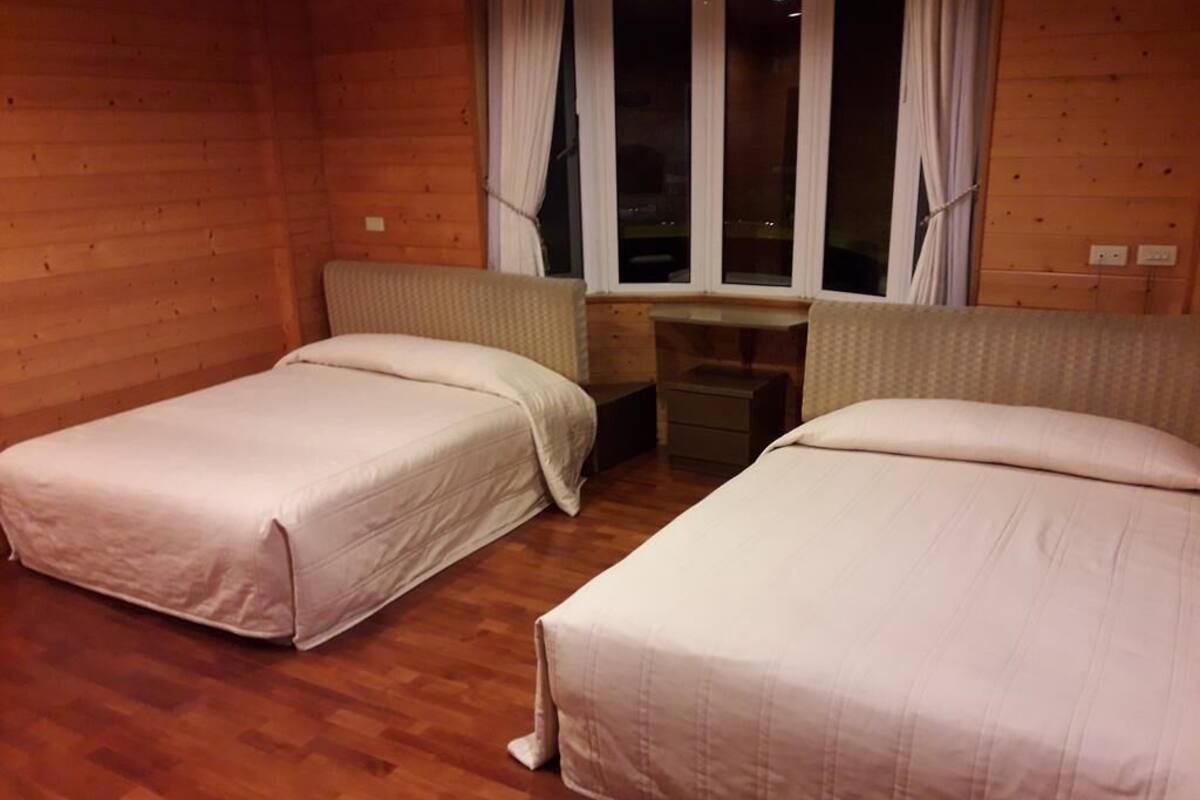A room with two beds, wooden walls, a small desk, and a window with curtains.