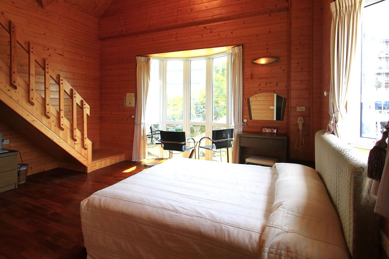 A wooden cabin room with a bed, a desk, and a chair.