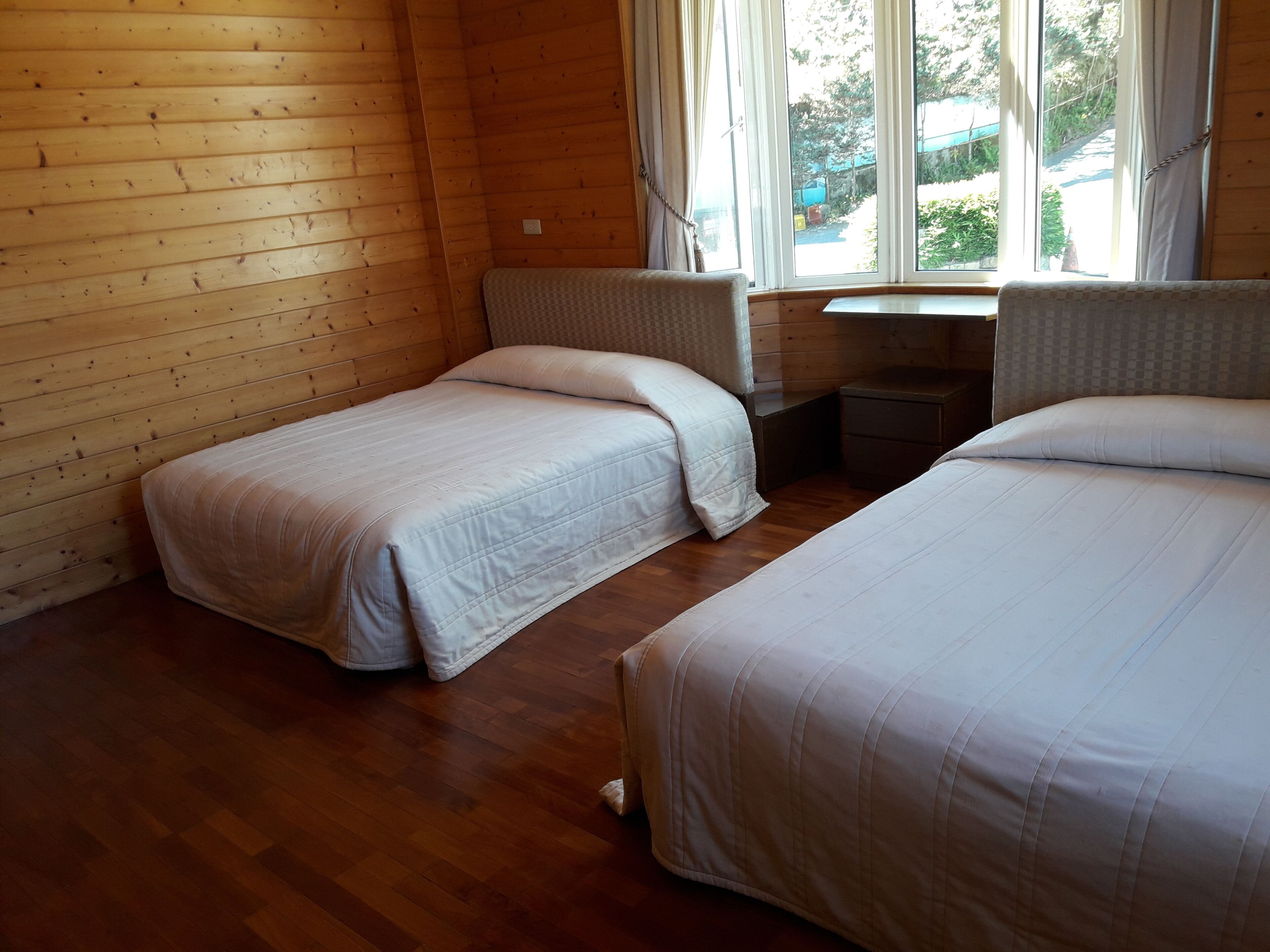 Una habitación con dos camas, paredes de madera, una ventana con cortinas y una mesita.
