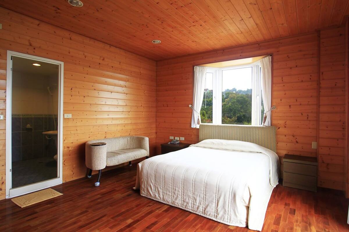 A wooden cabin bedroom with a bed, a sofa, a window, and a shower area.