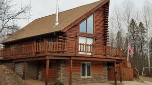 Une cabane en rondins dotée d’un balcon, avec des fondations en pierre et un drapeau américain.