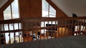 Une chambre à coucher aménagée dans un espace de type « loft », avec un plafond en pente, des poutres en bois et de grandes fenêtres.