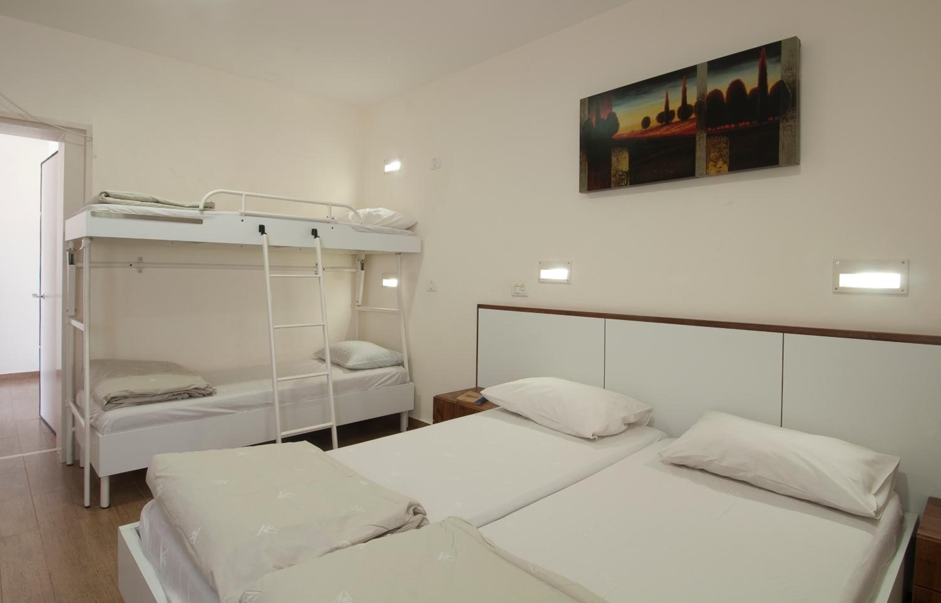 A room with bunk beds, a painting on the wall, and bedside lamps.