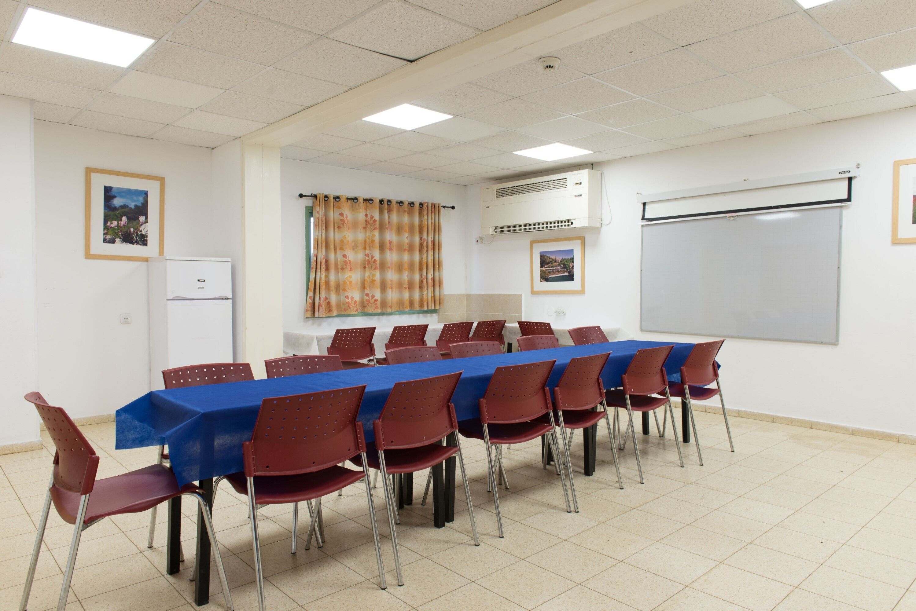 A conference room with a long table, red chairs, a blue tablecloth, a whiteboard, and an air conditioning unit.