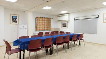 A conference room with a long table, red chairs, a blue tablecloth, a whiteboard, and an air conditioning unit.