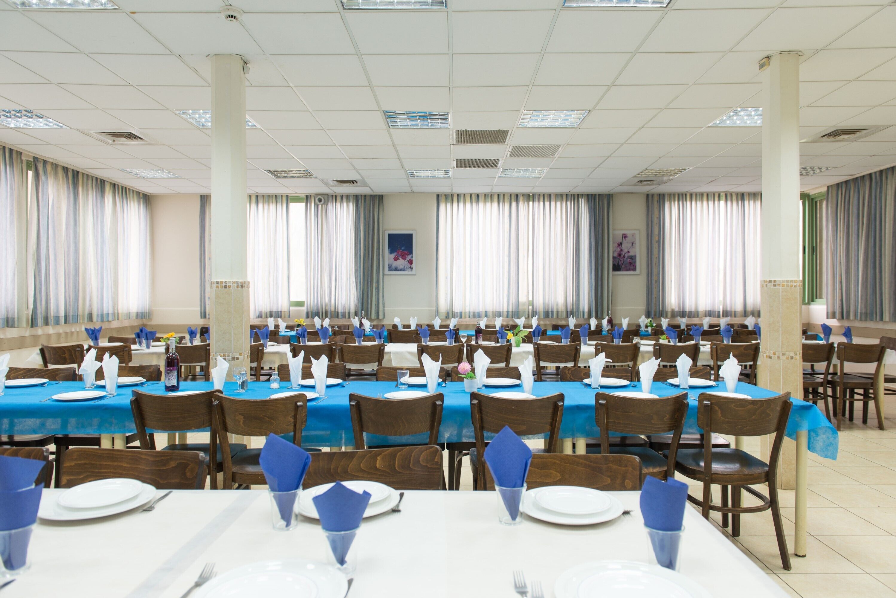 Une salle de banquet avec de nombreuses tables dressées pour le repas, ornées de nappes bleues et de assiettes blanches.