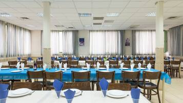 Une salle de banquet avec de nombreuses tables dressées pour le repas, ornées de nappes bleues et de assiettes blanches.