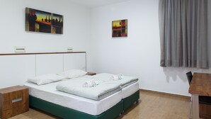 Hotelkamer met een tweepersoonsbed, twee nachtkastjes, een houten bijzettafeltje, een bureau en twee schilderijen aan de muur.