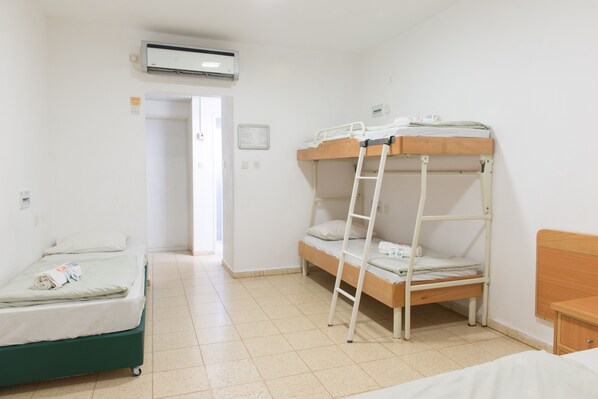 A room with bunk beds, a single bed, a ladder, an air conditioning unit, and a door leading to another room. - HI Maayan Harod Hostel (Gilboa)
