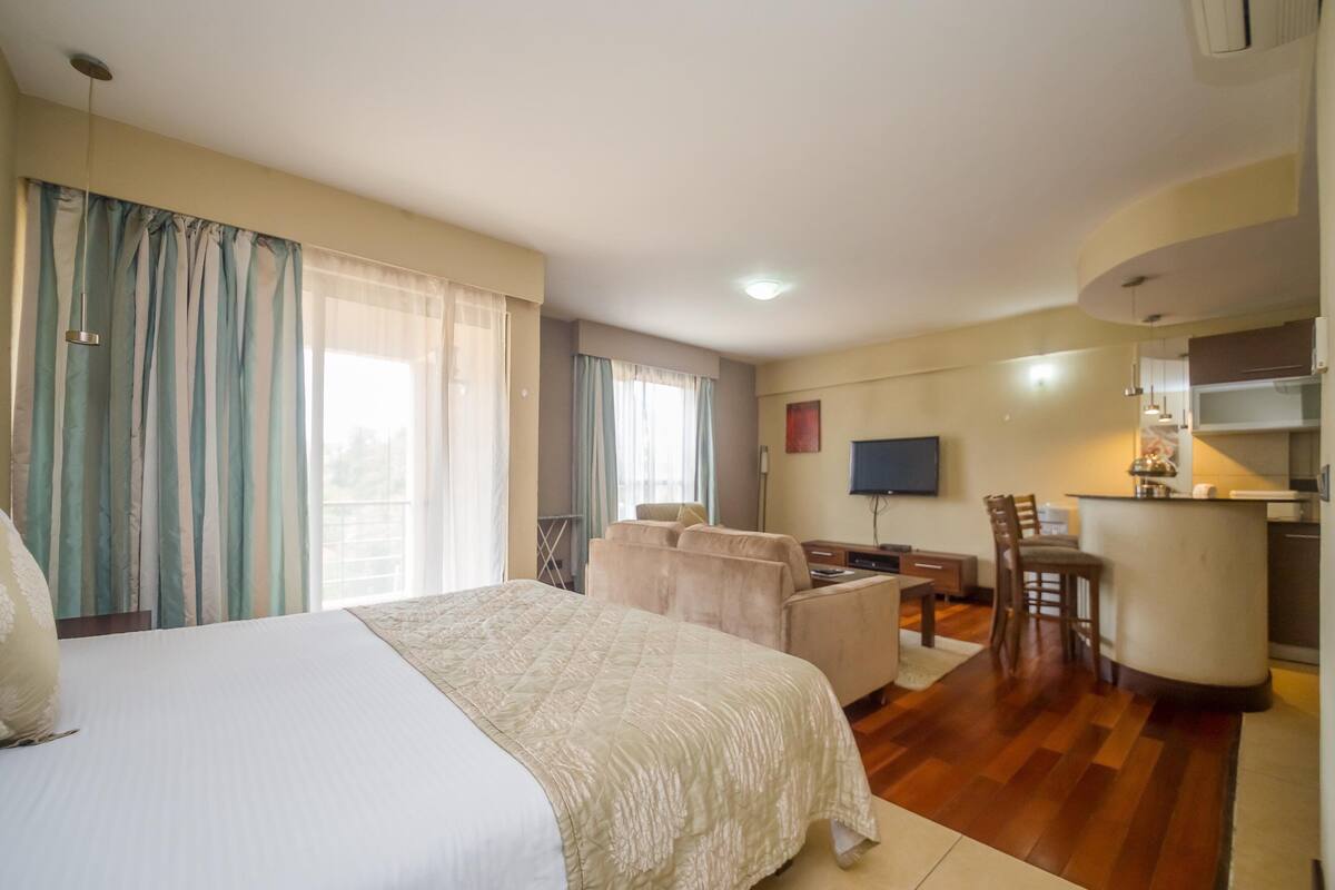 A hotel room with a bed, a sofa, a dining area, and a kitchen.