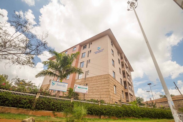 A multi-story building with balconies, a sign for "Taafifa Luxury Serviced Apartments," and a white fence with greenery. - Taarifa Suites by Dunhill Serviced Apartments (Nairobi)