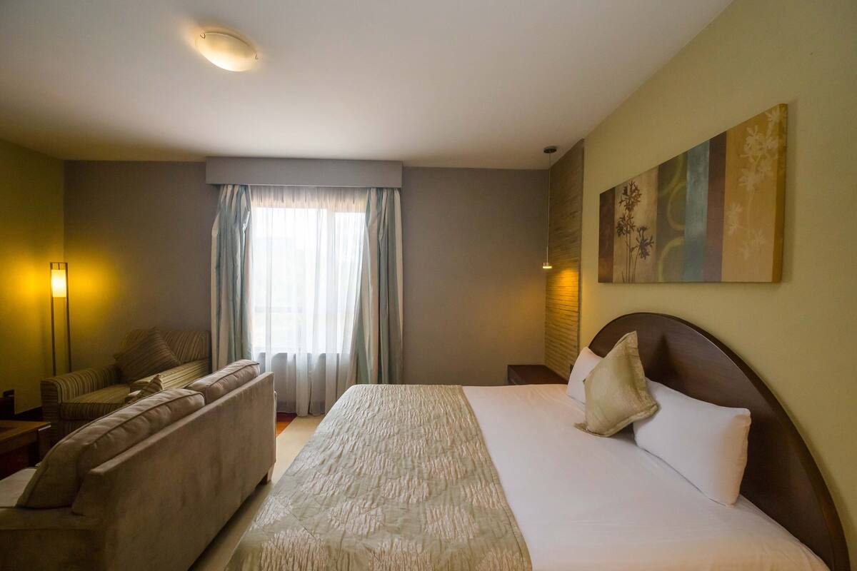 A hotel room with a large bed, a sofa, a desk, and a window with curtains.