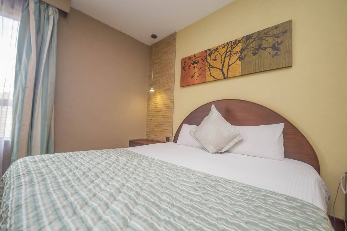 A neatly made bed with a patterned bedspread, a wooden headboard, and a wall-mounted painting.