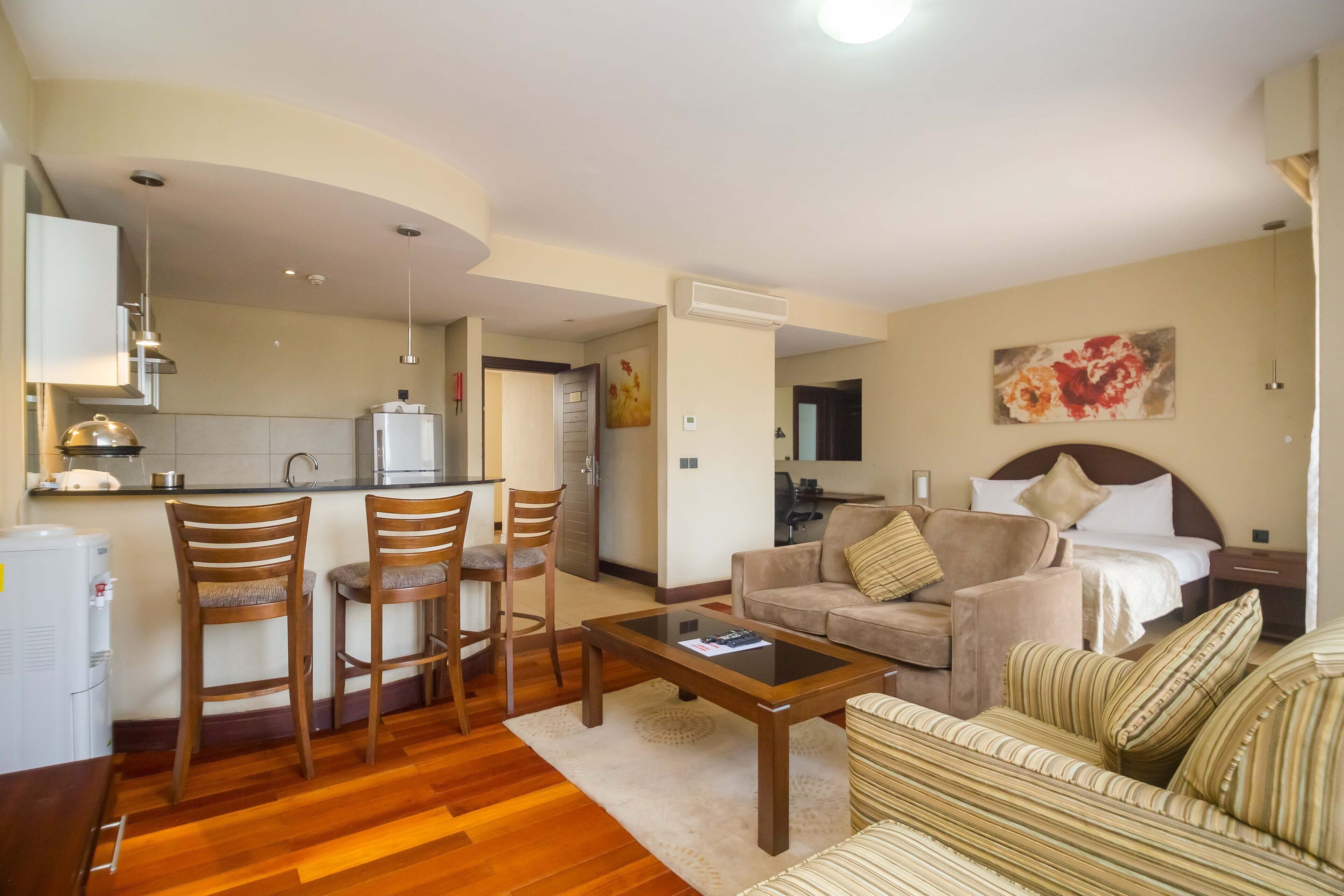 A modern living room with a sofa, armchairs, a coffee table, and a kitchen area with a refrigerator and microwave.