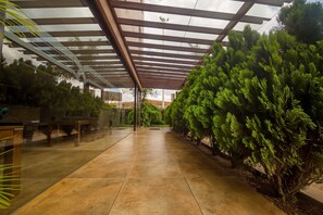 A covered walkway with tiled flooring, benches, and lush green trees. - Taarifa Suites by Dunhill Serviced Apartments (Nairobi)