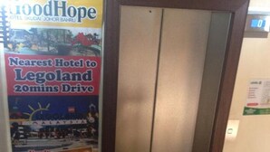A hotel entrance with a sign advertising the GoodHope Hotel, stating it's the nearest to Legoland with a 20-minute drive. There's a digital clock on the wall and a trash bin to the right. - Good Hope Hotel Kelana Jaya (Petaling Jaya)