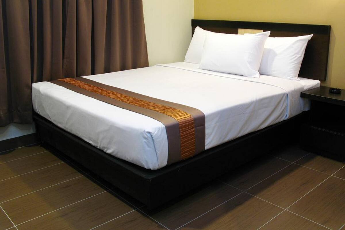 A hotel room with a large bed, a wooden headboard, and a nightstand with a lamp.