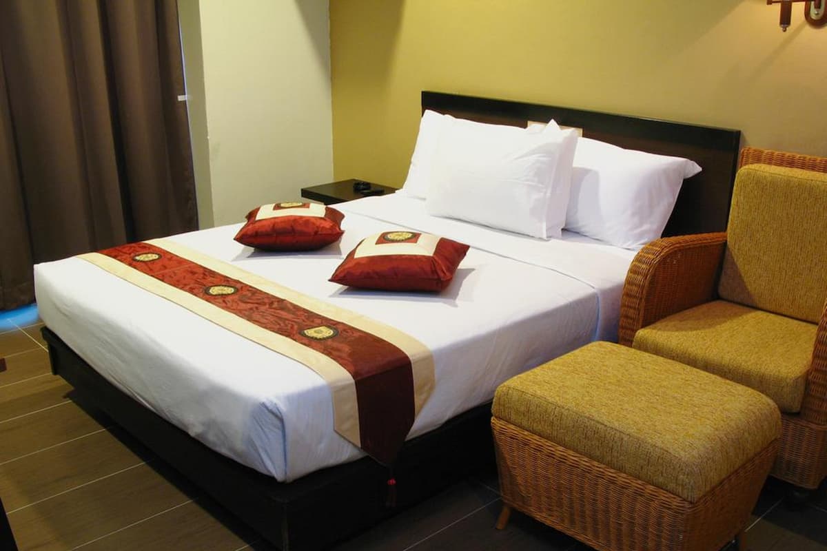A hotel room with a bed, two pillows, a nightstand, a chair, and a red and gold decorative bed runner.