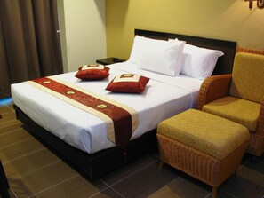 Ein Hotelzimmer mit einem Bett, zwei Kissen, einem Nachttisch, einem Sessel und einer rot-goldenen dekorativen Tagesdecke.