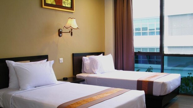A hotel room with two beds, a nightstand, a wall-mounted lamp, and a large window with a view of a building and greenery outside. - Good Hope Hotel Kelana Jaya (Petaling Jaya)