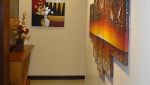 A hallway with a vase of flowers on a wooden table, a painting with a vase and flowers, and a textured abstract painting on the wall. - Good Hope Hotel Kelana Jaya (Petaling Jaya)
