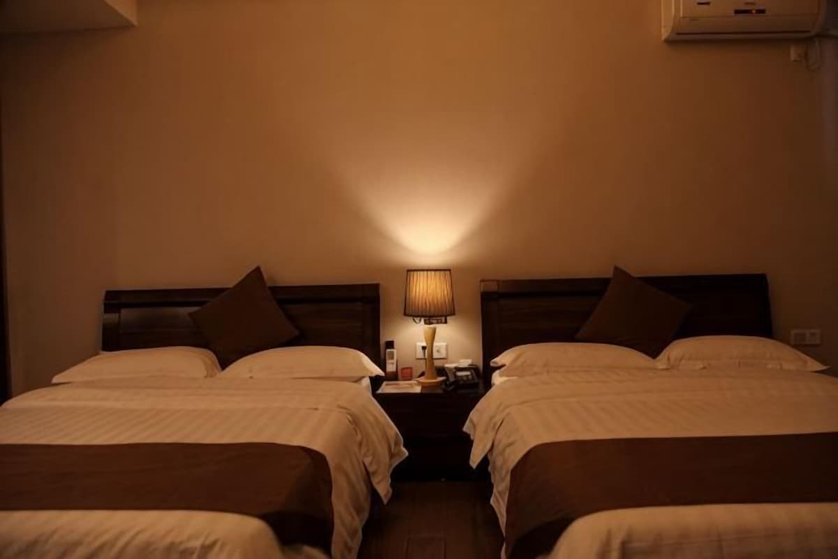 Una camera d'albergo con due letti, un comodino con una lampada e un condizionatore d'aria a parete.